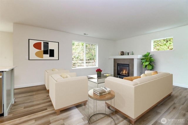 living area with light wood-style floors, a tile fireplace, and baseboards