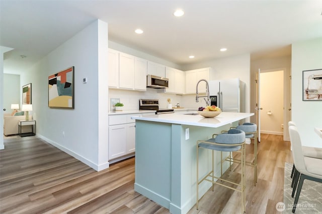 kitchen featuring white cabinets, light countertops, stainless steel appliances, light wood-style flooring, and a breakfast bar area