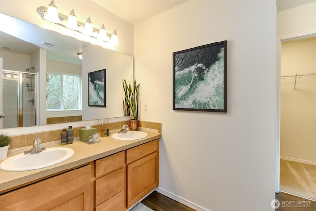 full bath with a stall shower, double vanity, a sink, and baseboards