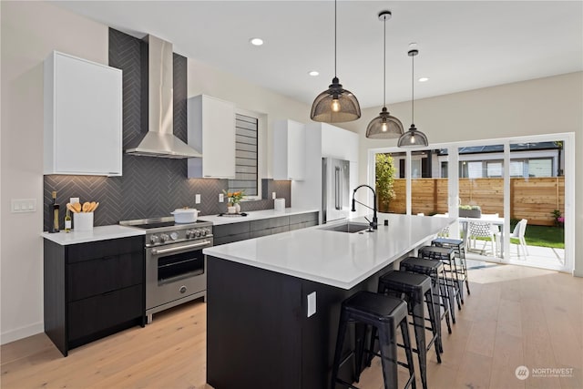 kitchen with pendant lighting, high end stove, an island with sink, sink, and wall chimney range hood