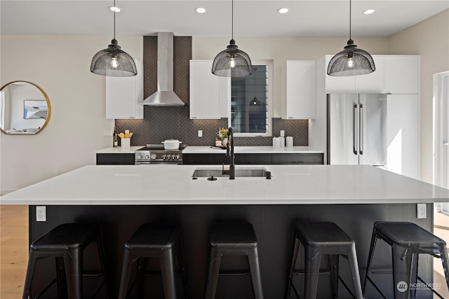 kitchen featuring wall chimney exhaust hood, sink, hanging light fixtures, high quality appliances, and an island with sink