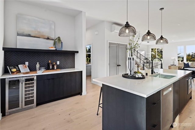 kitchen with pendant lighting, sink, tasteful backsplash, beverage cooler, and a large island with sink