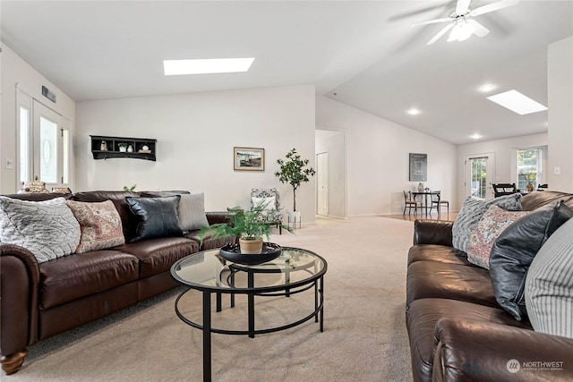 living room with vaulted ceiling with skylight, light colored carpet, and ceiling fan