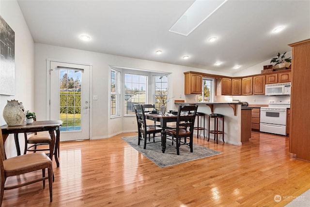 dining space with lofted ceiling with skylight and light hardwood / wood-style flooring