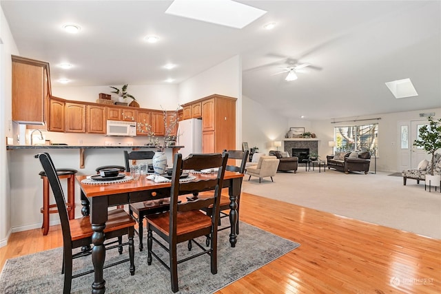 dining space with lofted ceiling with skylight, sink, ceiling fan, and light hardwood / wood-style flooring