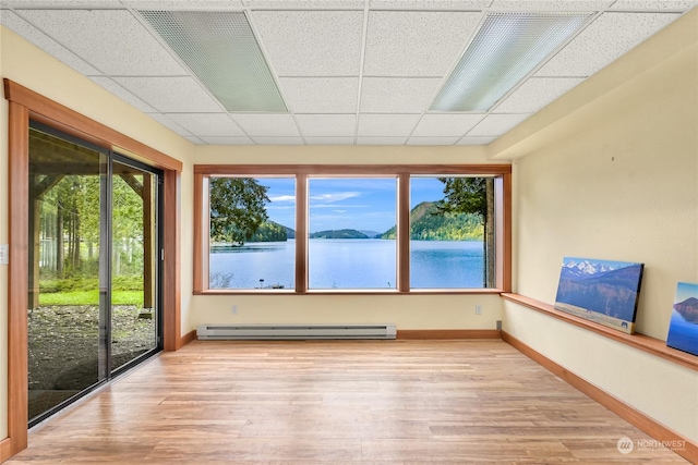 unfurnished sunroom featuring a drop ceiling, a baseboard heating unit, plenty of natural light, and a water view