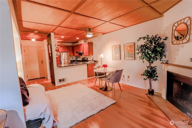 living room featuring a tiled fireplace, sink, wood ceiling, and light hardwood / wood-style floors