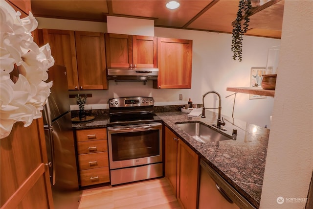 kitchen with stainless steel appliances, sink, light wood-type flooring, and dark stone counters