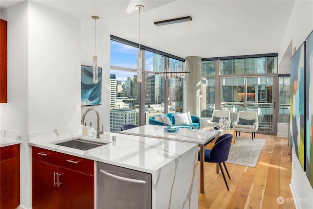 kitchen with pendant lighting, sink, expansive windows, light stone countertops, and light wood-type flooring