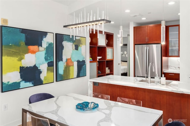 kitchen featuring pendant lighting, sink, stainless steel refrigerator, a kitchen breakfast bar, and light stone counters