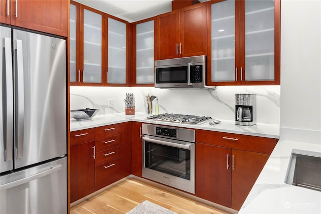 kitchen featuring stainless steel appliances, light stone countertops, decorative backsplash, and light wood-type flooring