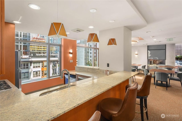 kitchen with sink, decorative light fixtures, carpet floors, and light stone countertops