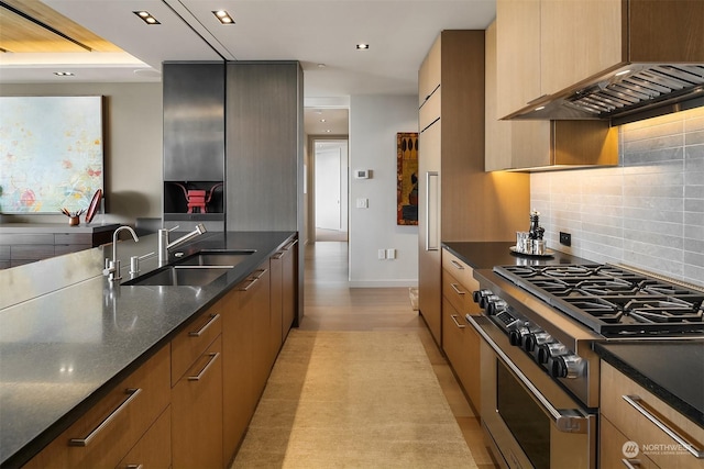 kitchen with sink, custom exhaust hood, dark stone counters, high end stove, and backsplash