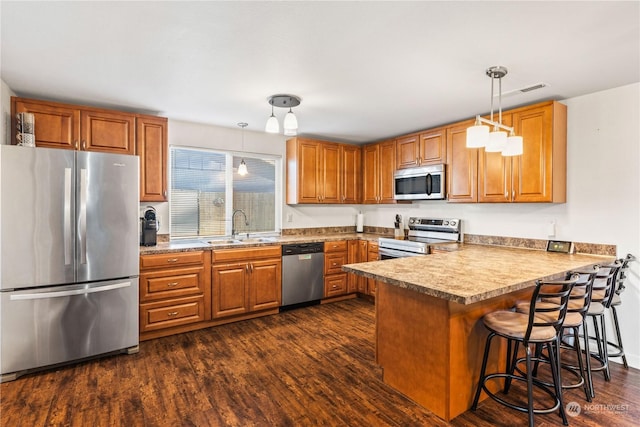 kitchen with appliances with stainless steel finishes, pendant lighting, sink, a kitchen breakfast bar, and kitchen peninsula