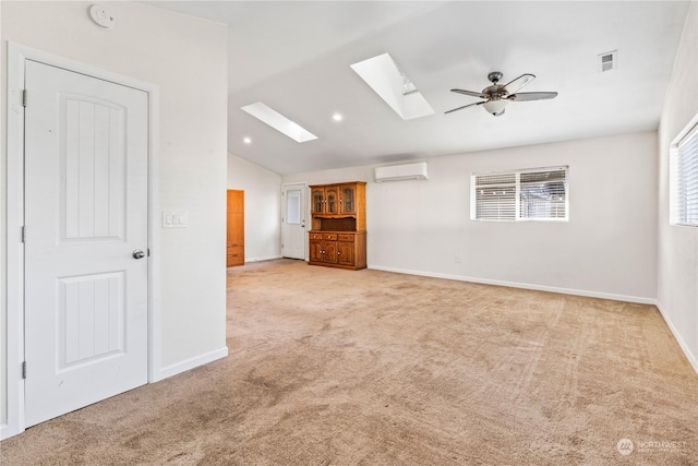 empty room with a wall mounted air conditioner, light colored carpet, vaulted ceiling with skylight, and ceiling fan