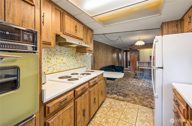 kitchen with hanging light fixtures, white appliances, wooden walls, and light colored carpet