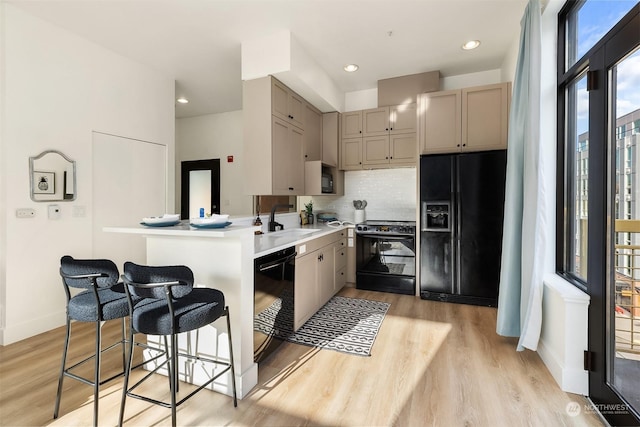 kitchen with a kitchen bar, sink, light hardwood / wood-style floors, decorative backsplash, and black appliances