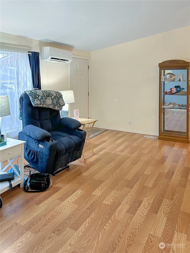 living area with a wall unit AC and light hardwood / wood-style flooring