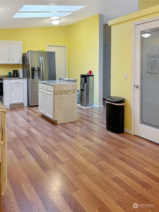 kitchen with stainless steel refrigerator with ice dispenser, vaulted ceiling with skylight, light hardwood / wood-style floors, and white cabinets