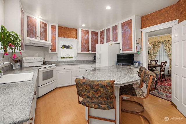 kitchen featuring sink, a kitchen breakfast bar, light stone counters, white appliances, and light hardwood / wood-style flooring