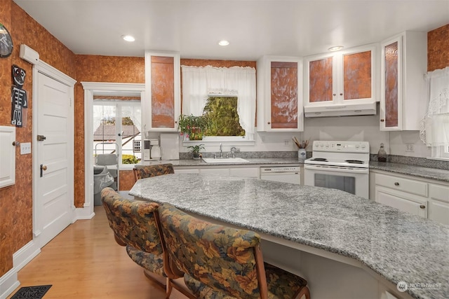 kitchen with white appliances, a breakfast bar, sink, and white cabinets