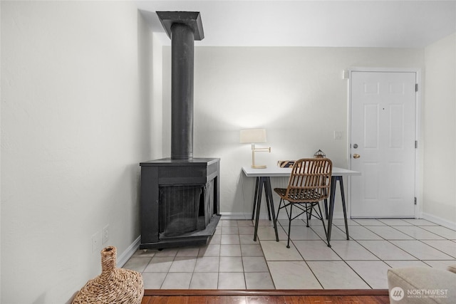 dining space featuring a wood stove, light tile patterned floors, and baseboards