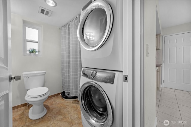 bathroom with baseboards, visible vents, stacked washer and clothes dryer, toilet, and tile patterned floors