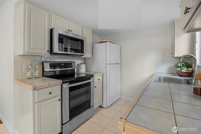 kitchen featuring light tile patterned floors, stainless steel appliances, a sink, tile counters, and decorative backsplash