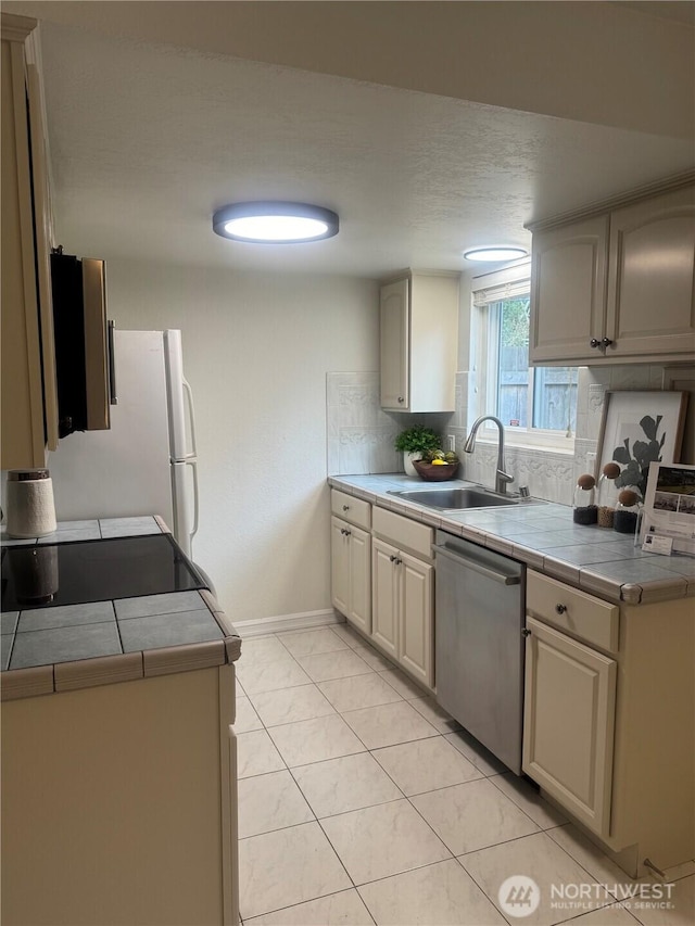 kitchen featuring tile countertops, a sink, baseboards, stainless steel dishwasher, and backsplash