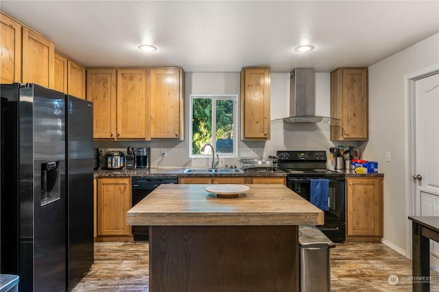 kitchen featuring wall chimney exhaust hood, butcher block counters, sink, a center island, and black appliances