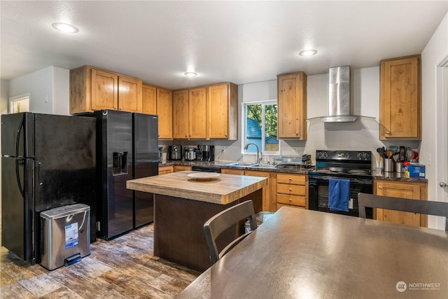 kitchen featuring sink, hardwood / wood-style flooring, black appliances, a kitchen island, and wall chimney exhaust hood