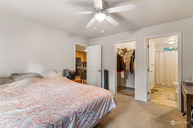 bedroom with connected bathroom, a walk in closet, light colored carpet, a closet, and ceiling fan