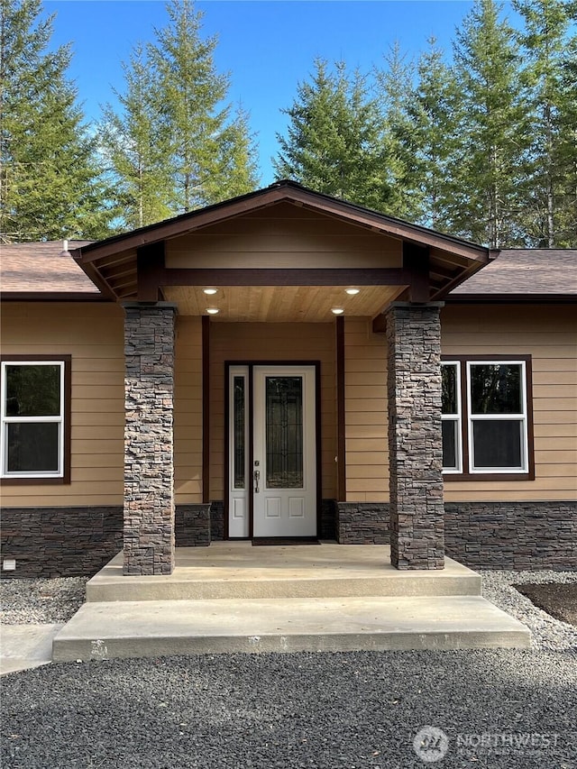 property entrance featuring stone siding and roof with shingles