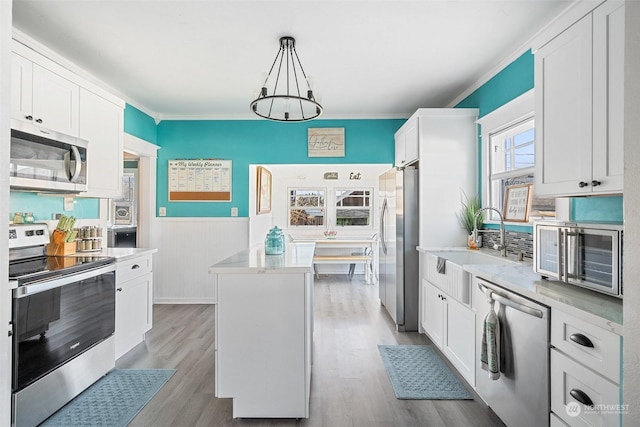 kitchen featuring appliances with stainless steel finishes, a center island, white cabinets, and decorative light fixtures