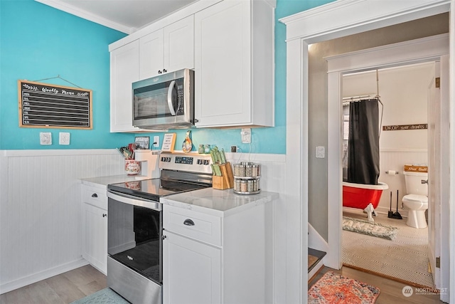 kitchen with white cabinetry, light stone counters, light hardwood / wood-style flooring, ornamental molding, and stainless steel appliances