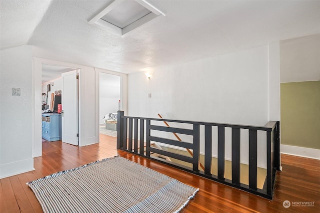 hallway featuring lofted ceiling, wood-type flooring, and a textured ceiling