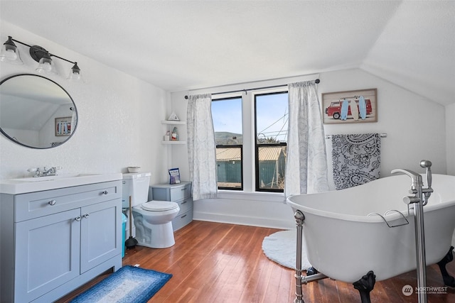 bathroom with vaulted ceiling, hardwood / wood-style floors, a tub to relax in, vanity, and toilet