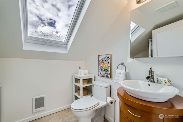 bathroom featuring heating unit, vanity, lofted ceiling with skylight, and toilet