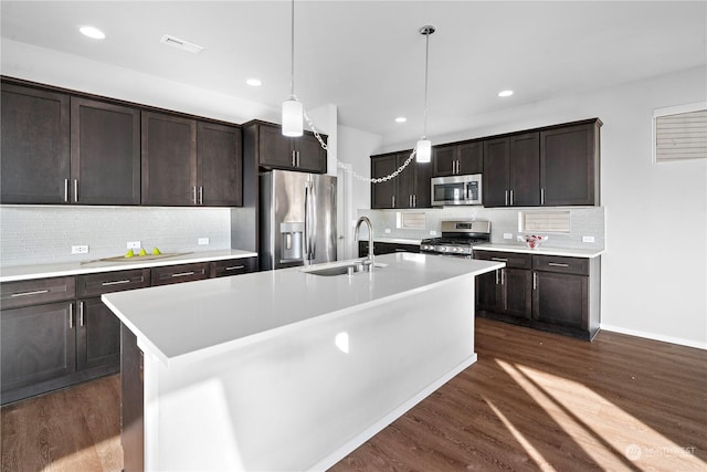 kitchen featuring an island with sink, stainless steel appliances, dark brown cabinetry, sink, and pendant lighting