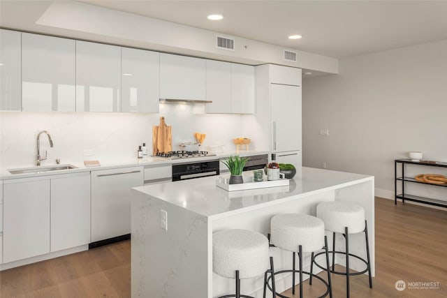 kitchen featuring sink, black oven, a kitchen island, stainless steel gas stovetop, and white cabinets