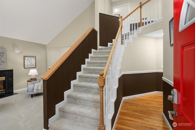 staircase with high vaulted ceiling, a fireplace, baseboards, and wood finished floors