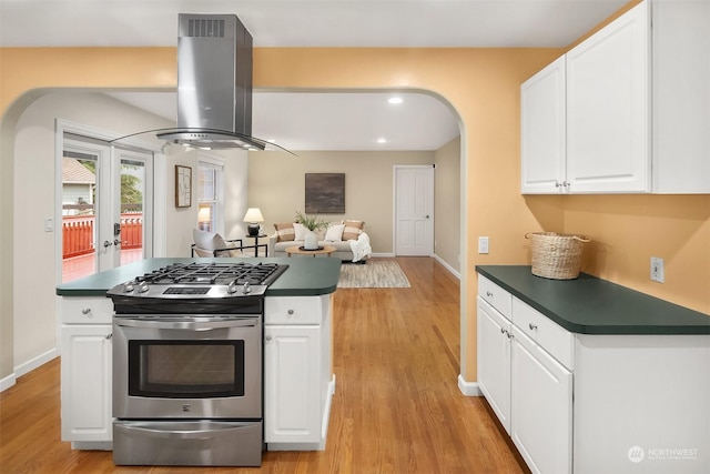 kitchen with dark countertops, stainless steel range with gas stovetop, island exhaust hood, and white cabinetry