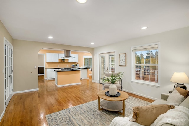 living area featuring arched walkways, light wood finished floors, baseboards, and recessed lighting