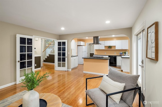 living room featuring arched walkways, recessed lighting, light wood-type flooring, baseboards, and stairs