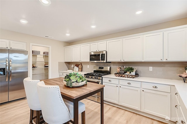 kitchen featuring decorative backsplash, stainless steel appliances, light hardwood / wood-style floors, and white cabinets