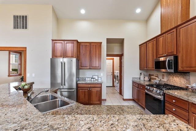 kitchen with sink, washer and clothes dryer, a towering ceiling, stainless steel appliances, and light stone countertops