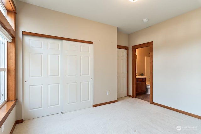 unfurnished bedroom featuring a closet, ensuite bathroom, and light carpet