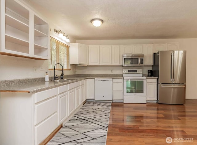 kitchen featuring appliances with stainless steel finishes, a sink, light wood-style floors, white cabinets, and a textured ceiling