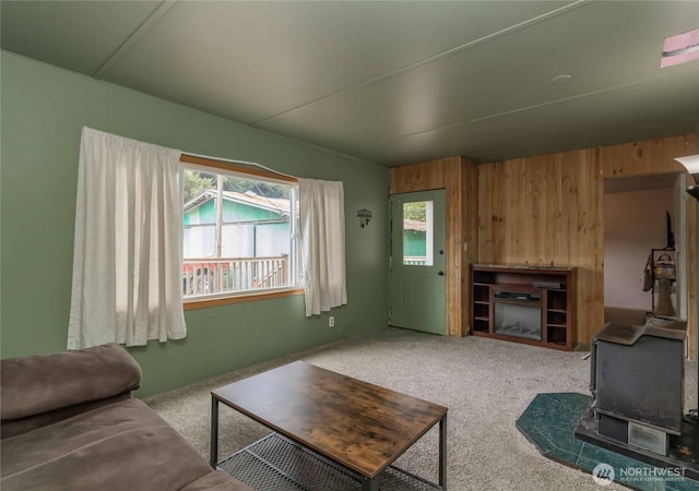 carpeted living area featuring a wood stove, healthy amount of natural light, and wood walls