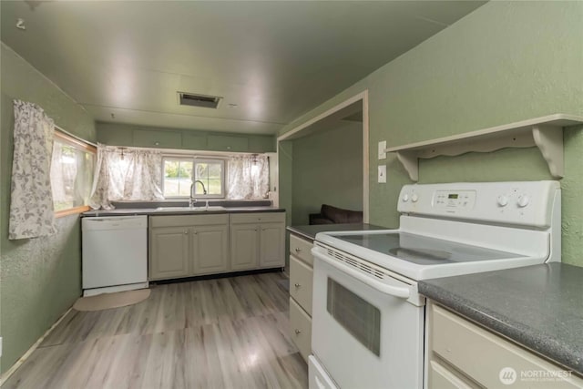 kitchen with white appliances, a sink, dark countertops, light wood-style flooring, and a textured wall